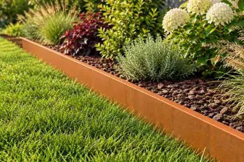 Corten steel garden edging separating a lawn from a flower bed with ornamental grasses